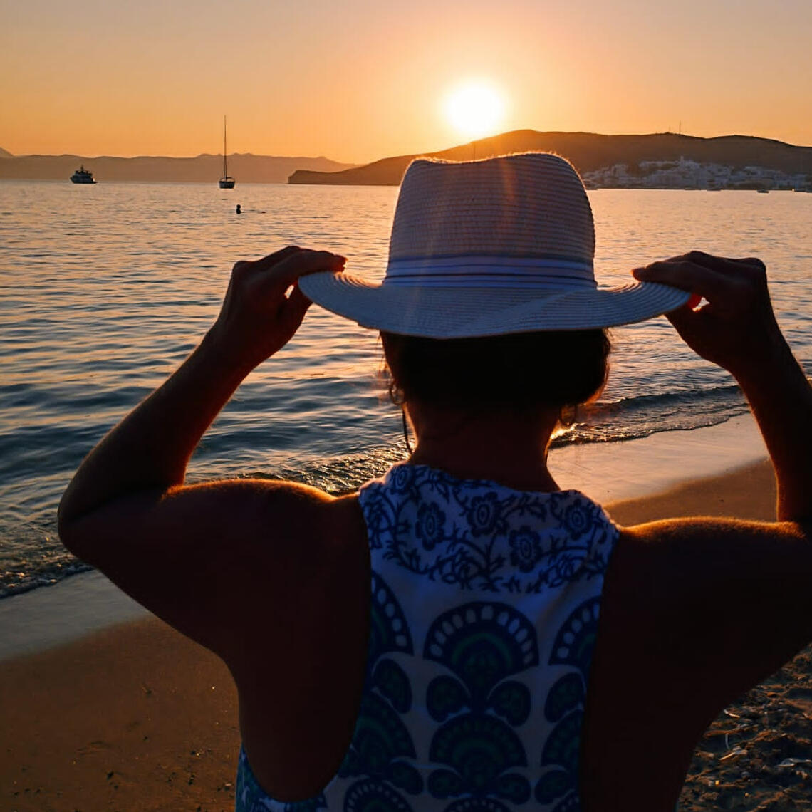 Lady on the beach in Milos Greece looking at the sunset having a photoshoot done. She is wearing a hat