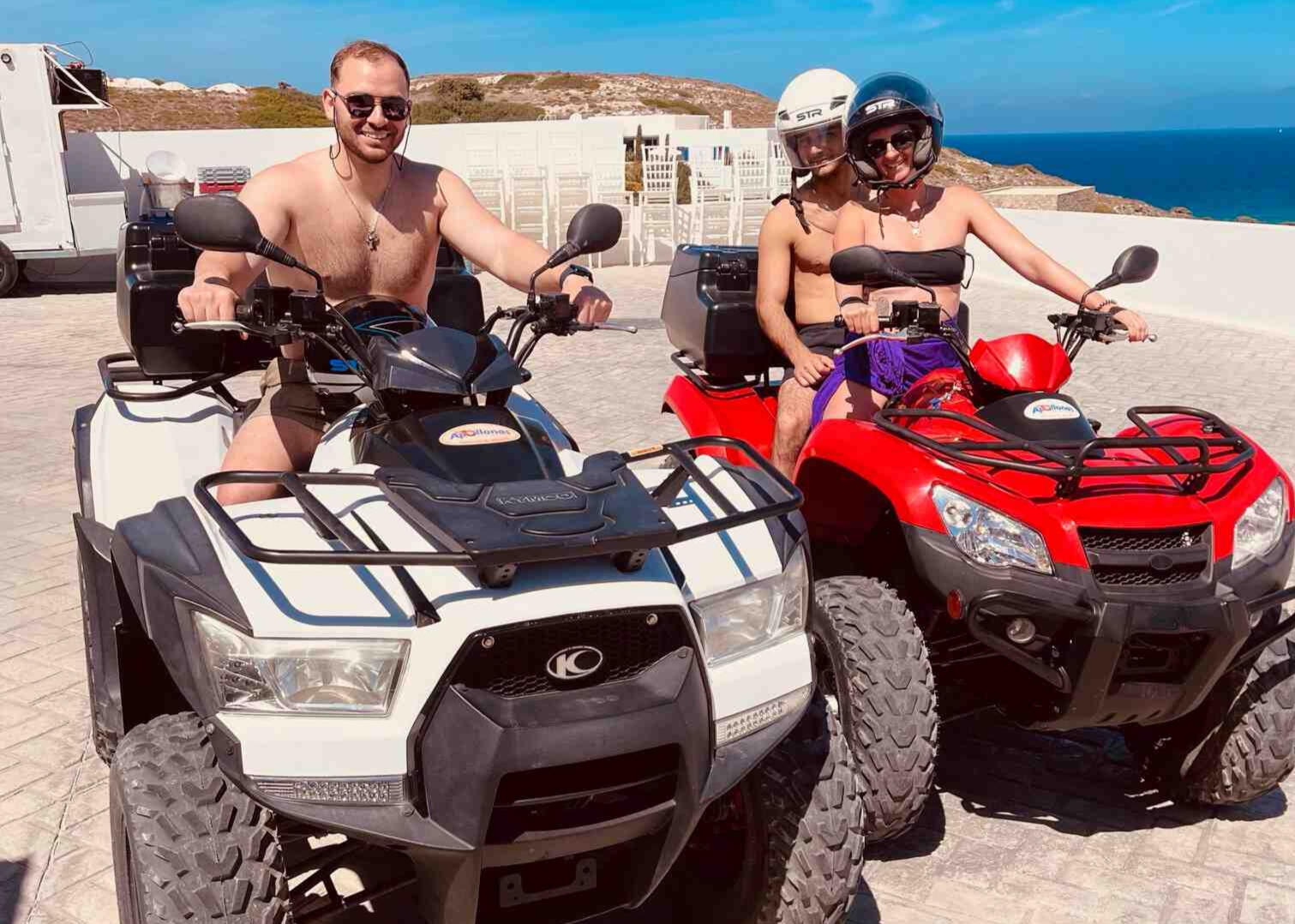 3 people on ATV in Milos Greece, photo taken by Mia's Photography and Events. One white ATV, one red ATV. Smiling for a photo sh